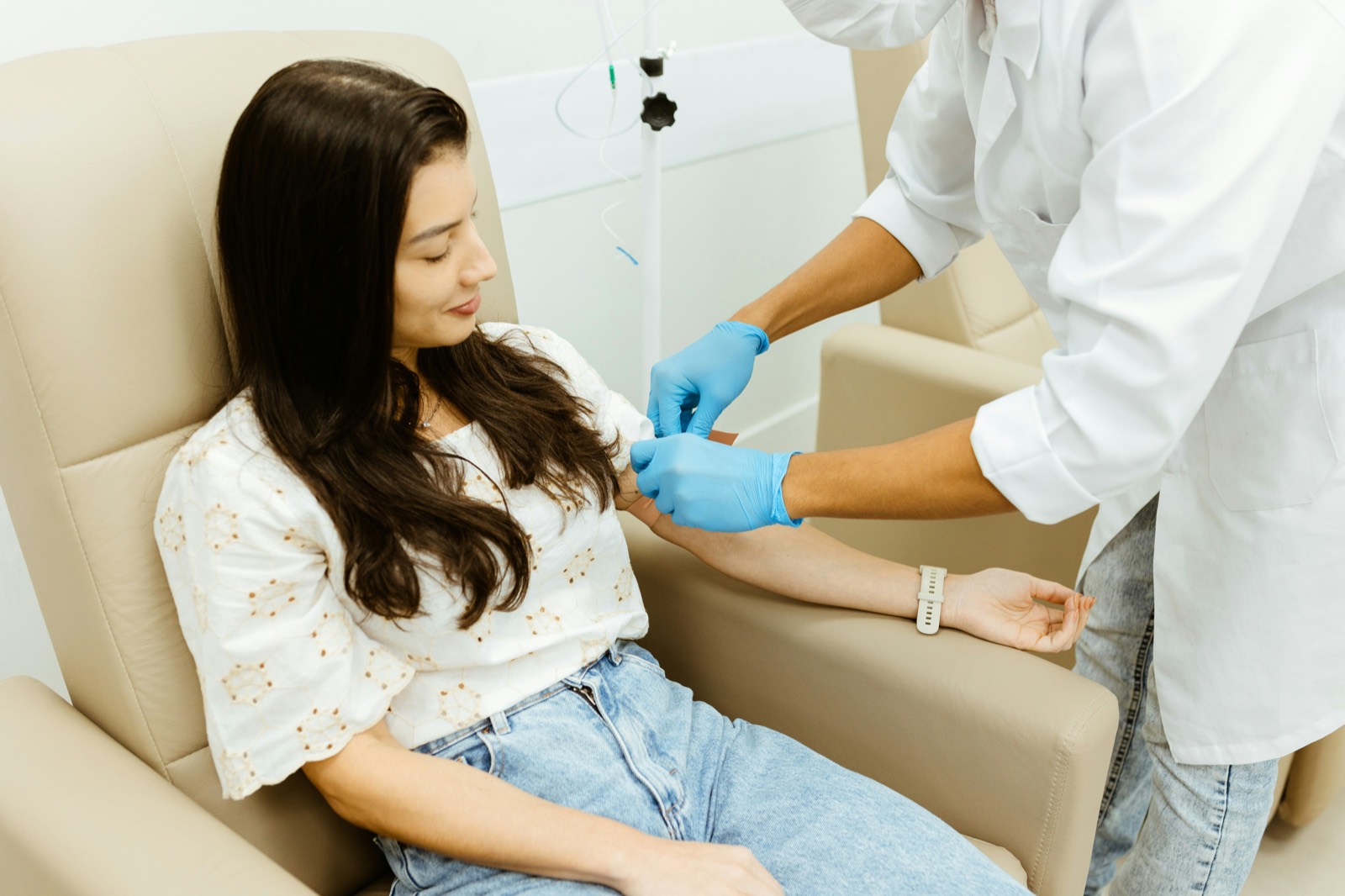 A nurse in gloves prepares an IV line in a patient's arm