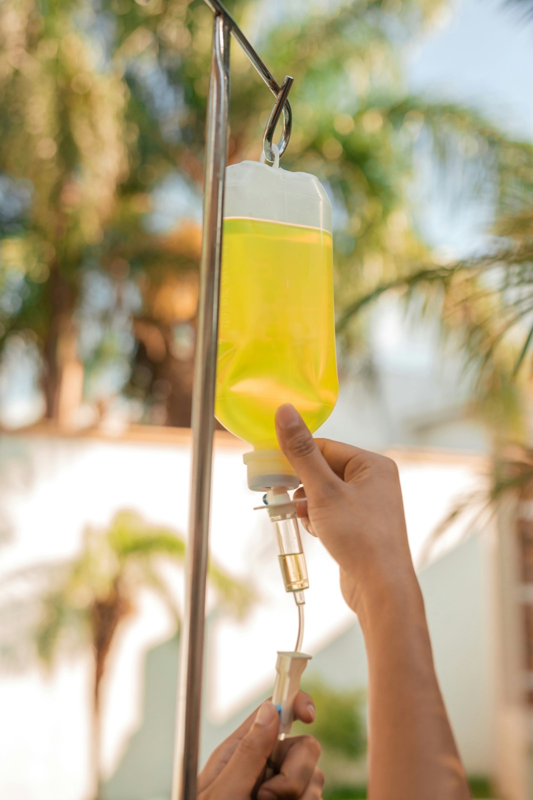 A yellow IV bag hangs outdoors among palm trees in Phuket